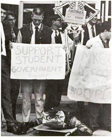 From the 1967 Bugle, a photograph of a demonstration anchored by a student clad in a cockroach costume and carried around on a stretcher.