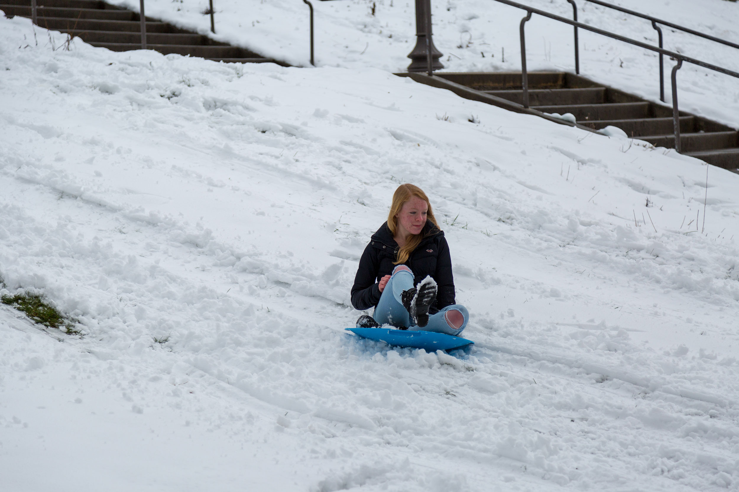 A student slides down a hill on a snow day in March.